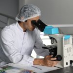 Scientist in a lab, looking down a telescope at the samples sent to test for a food intolerance