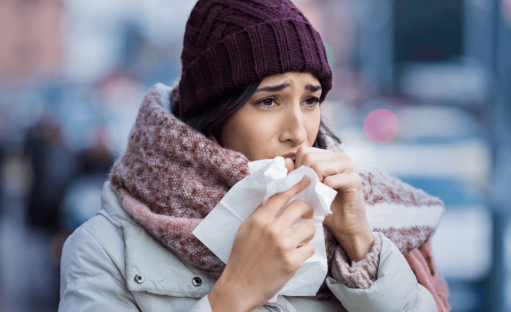 A woman dressed in winter clothes coughing and covering her face with a tissue